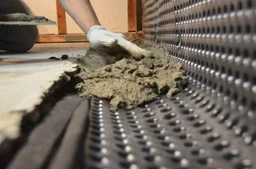 Interior basement drainage membrane being installed along a foundation wall